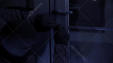 trespassing, male thief in gloves using picklocks trying to pick a lock and open a door to a room at night, close-up