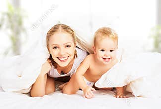 Happy family mother and baby under blankets in bed
