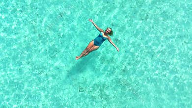 Woman floating in crystal clear turquoise water, arms stretched, enjoying relaxation on tropical island, peaceful