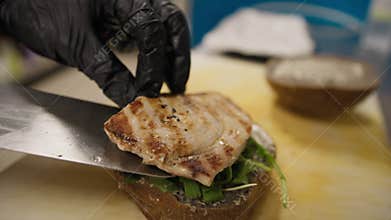 Chef Adding Grilled Swordfish On Top Of The Vegetables Preparing A Burger