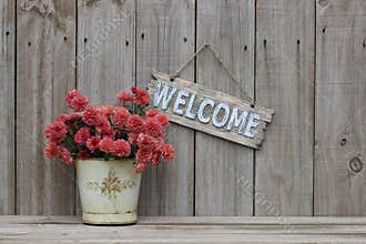 Wood welcome sign with pot of flowers by wooden fence
