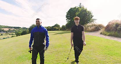 Two male golf players playing golf together, walking with clubs on a golf course on a sunny day