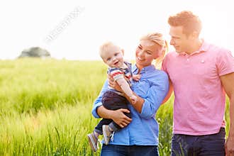 Family Walking In Field Carrying Young Baby Son