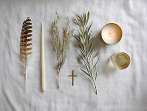Reverent arrangement of dove feather, olive branch, candle, and cross on soft linen cloth