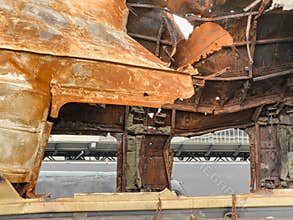 Burned-out train car ruins, advanced decay, rusted metal body, collapsed structure, inner framework exposed, outdoor junkyard
