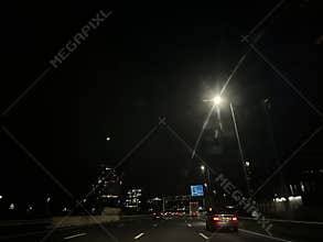 Night highway traffic under bright streetlights with city skyline in distance
