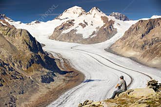 Young man sitting and enjoying a majestic view to Aletsch glacier, the largest gracier in Alps and UNESCO herritage from
