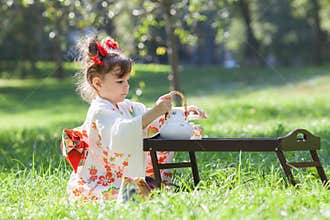 The small girl in kimono is sitting on the grass