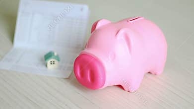 Close up shot hand of man putting money coin into pink piggy bank and blur home and book bank passbook behind metaphor of saving m