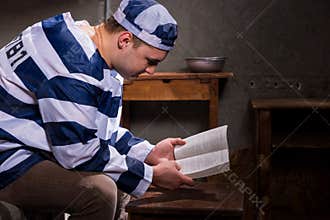 Young male prisoner wearing prison uniform reading a book or a b