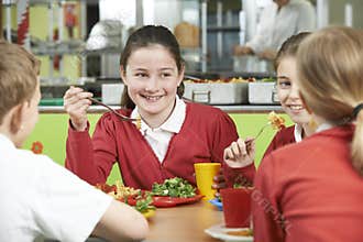 Group Of Pupils Sitting At Table In School Cafeteria Eating Lunc