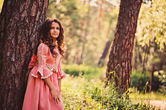 Happy curly child girl in fairytale princess pink dress on the walk in summer forest