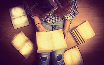 Girl in a shirt holding a book sitting on the floor around her spread open books close up retro toning