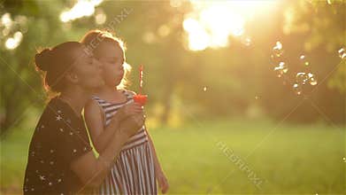 Beautiful mother with her daughter in nature making soap bubbles and laughing