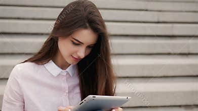 Young beautiful student girl using a tablet computer outside. Pretty teen woman reading on air.