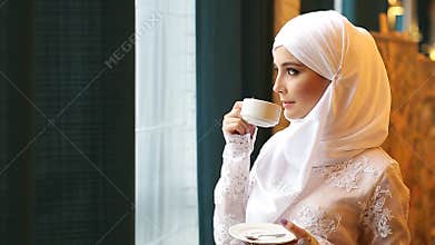 Muslim woman in a white wedding dress with a cup of tea in his hands