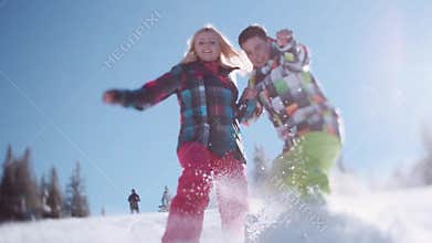 Happy couple in colorful ski costumes. Floor level shooting of joyful young people sliding in the snow towards the