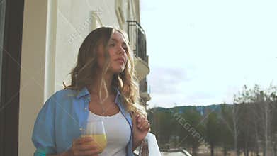 Woman on the balcony in the early morning and drinks orange juice.