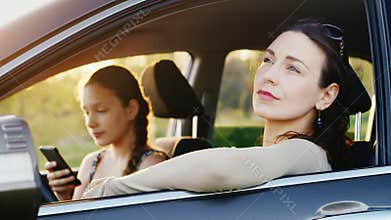 Mom and daughter 11 years old rest in the car in a picturesque place at sunset. A woman is looking at the car window
