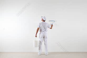 Rear view of painter man looking at blank wall, with paint roller and bucket, isolated on white room