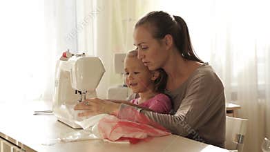 Young attractive mother working on sewing machine with her little cute daughter