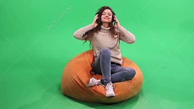 Girl with curly hair sitting on bean bag and listening music