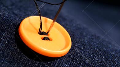 Sewing an orange button on jeans, denim, close up