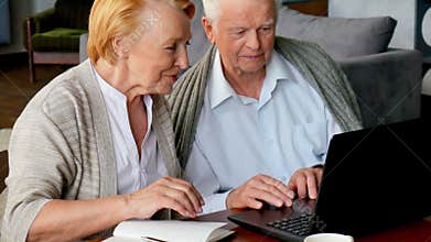 Senior couple websurfing on internet with laptop. Happy elderly man and woman using computer