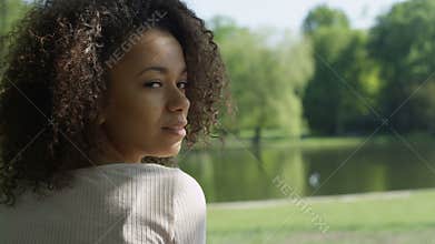 Young beautiful mixed race woman with curly afro hair smiling happily in a green park.