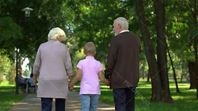 Old couple walking with boy in park, holding hands, adoption social support