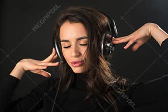 Close-up portrait of young beautiful brunette woman listening to music with her eyes closed and holding headphones over