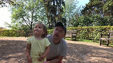 Father and little daughter look to sky in summer park in day