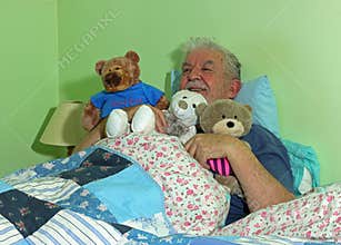 Senior man in bed with soft cuddly toys.