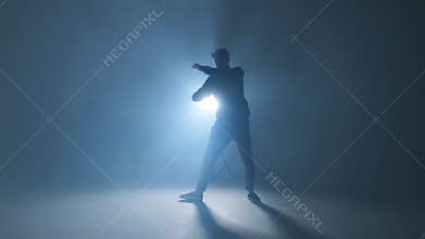 Young man dancer dancing funky hip hop on isolated studio neon blue background, slow motion