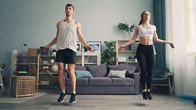 Young man and woman couple jumping rope in house together doing sports indoors