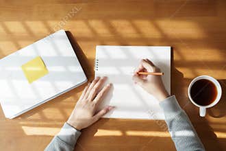 Asian women are taking notes on wooden table with coffee mugs and laptops at home