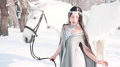 Charming gorgeous dark princess in a fabulous winter forest with white pegasus, a brave model poses for the camera in
