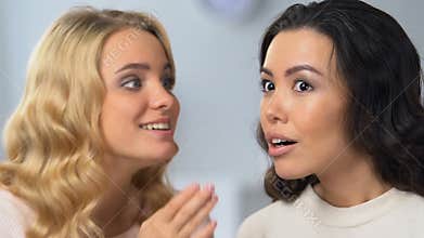 Pretty blonde girl whispering secrets to her attractive asian friend, gossips