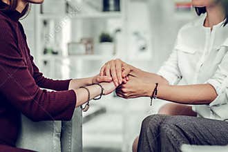 Psychologist wearing white shirt and bracelets holding hands of client
