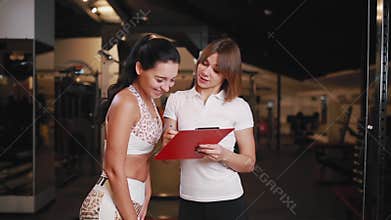 Female personal trainer talking to a woman client in a gym using a tablet for notes.