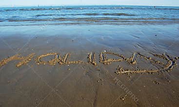 Word Holiday written in the sand