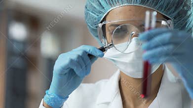 Female medical worker looking at blood test through magnifying glass, analysis