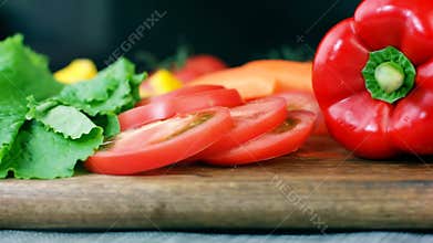 Salad leaves, cutted tomato, bell pepper and carrot on wooden board, making healthy vegetable salad, dolly shot