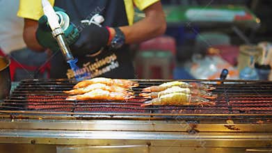 Street food asia, traditional Asian dishes. seafood shrimp on the grill, the cook toast their burner. night food market