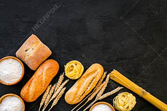 Farinaceous food. Fresh bread and raw pasta near flour in bowl and wheat ears on black background top view copy space