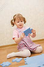 Little girl collects puzzles in a room