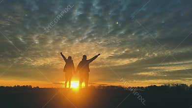Silhouettes of two hikers with backpacks enjoying sunset view from top of a mountain. Enjoying the sunset view from