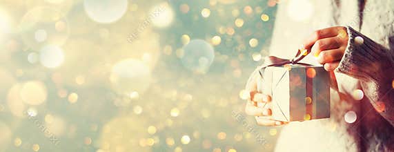 Shimmer background with snow, light bokeh. Woman hands opening gift box. Christmas, new year, birthday concept. Banner, copy space