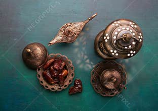 Bronze plate with dates, coffee cup, arabic lantern and aladdin lamp on dark green wooden background. Ramadan kareem. Ramadan