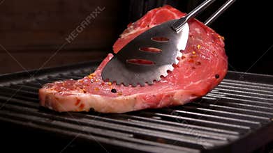 Cook puts steak using tongs on the grill grate